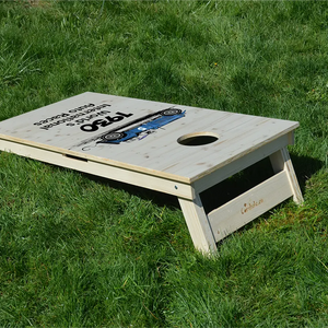 cornhole motif personnalisable sur fond de bois naturel, sur le gazon, vue de derrière