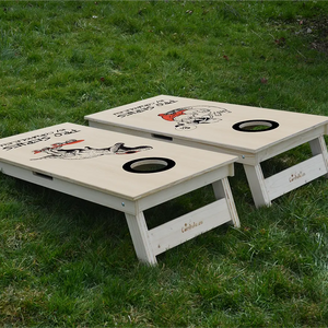 cornhole de compétition deux planches hipster et t-rex sur son skate, sur le gazon, vue de derrière