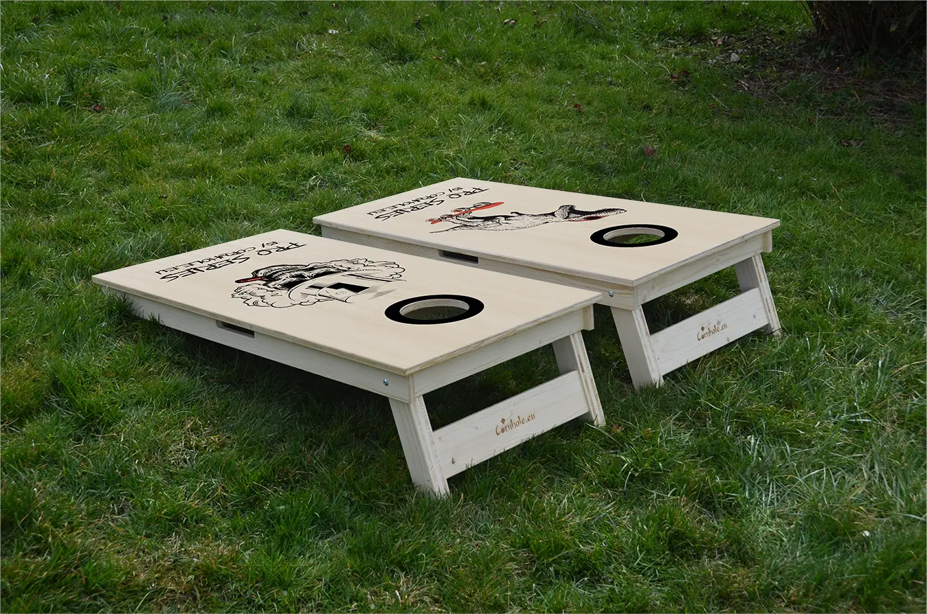 cornhole de compétition deux planches t-rex sur son skate et tête de mort, sur le gazon, vue de derrière