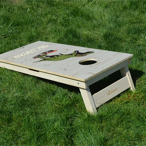 cornhole t-rex à lunettes sur un skateboard, sur le gazon, vue de derrière