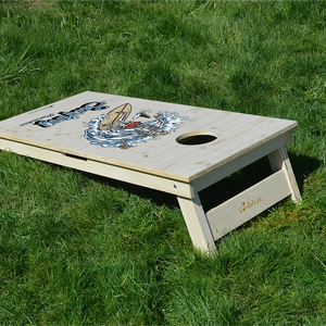 cornhole squelette surfant une vague à coté d'un requin, sur le gazon, vue de derrière